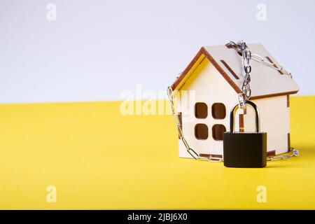 Arresto dell'alloggiamento. Casa del castello. Piccola casa giocattolo e una catena con un lucchetto. Sfratto per mancato pagamento. La porta chiusa a chiave della casa. Foto Stock