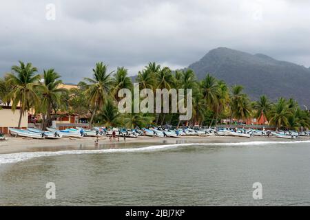 Vista panoramica delle barche da pesca sulla spiaggia con palme e colline a Zihuatanejo, Messico Foto Stock