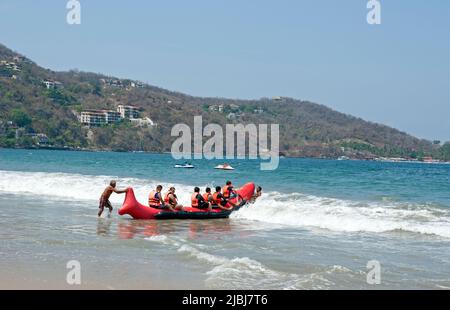 I visitatori di Playa la Ropa si preparano a fare un giro su una grande barca gonfiabile a Zihuatanejo, Messico Foto Stock