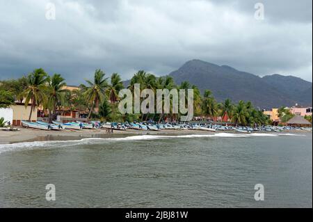 Vista panoramica delle barche da pesca sulla spiaggia con palme e colline a Zihuatanejo, Messico Foto Stock