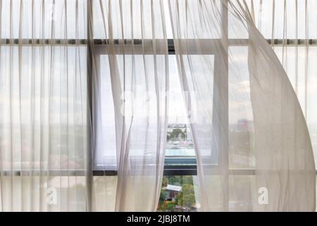 Le tende sbatte nel vento da una finestra aperta in una parete di finestre quadrate Foto Stock