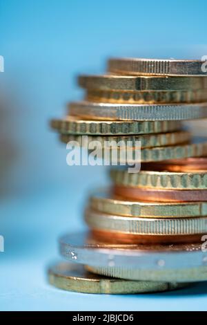 Monete in euro accumulate in una torre, primo piano della moneta in euro. Sfondo blu dietro la torre delle monete Foto Stock