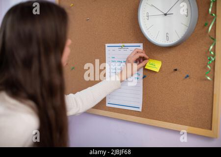 Un adolescente tape un pezzo di carta sul tabellone con una parola scritta in inglese. Foto Stock