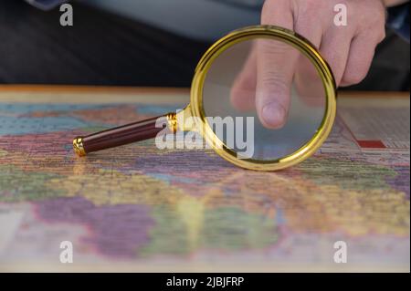 Un uomo tiene una lente d'ingrandimento in mano sopra una mappa. Uomo di mezza età con una lente d'ingrandimento in una cornice d'oro. I nomi sono scritti in ucraino. Foto Stock