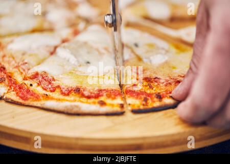 Tagliare una pizza con un taglierino rotondo. Vista frontale. Foto Stock