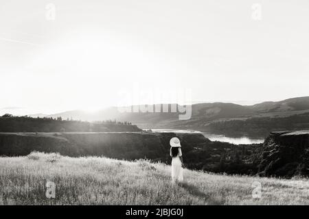 Una ragazza con lunghi capelli scuri che si affaccia su una valle del fiume che indossa un cappello Foto Stock