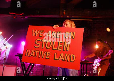 Bloomington, Stati Uniti. 03rd giugno 2022. Merrill Garbus di Tune-yards detiene un segno che dice, "Siamo sulla terra nativa rubata," mentre si esibisce al Bluebird durante il festival Granfalloon. Granfalloon è un festival annuale di arti, musica e borse di studio ispirate dall'autore di Hoosier Kurt Vonnegut, secondo la pagina web degli eventi. Il festival si svolge a Bloomington, Indiana. Credit: SOPA Images Limited/Alamy Live News Foto Stock