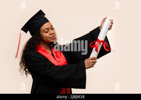 Lo studente delle scuole superiori afro-americane celebra la laurea e si rallegra di ricevere il certificato di istruzione. Ragazza con pelle scura in muratura e gradu Foto Stock