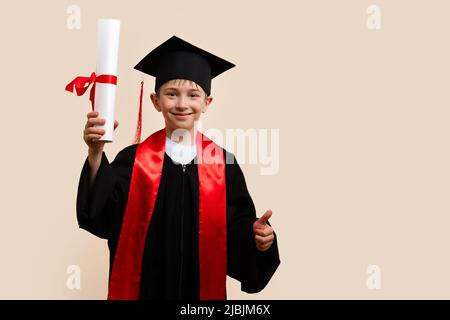 Ragazzo di 9-11 anni con cappuccio di laurea e abito da cerimonia con certificato di diploma legato con nastro rosso in studio. Laureato per celebrare la laurea Foto Stock