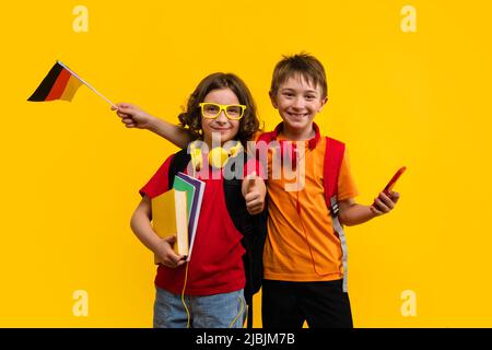 Fratello e sorella 9-11 y.o in Basic T-shirt in posa su sfondo giallo. Due bambini della scuola con le cuffie contengono i libri di testo gli smartphone e. Foto Stock