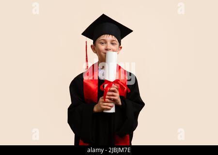 Capretto di whizz 9-11 anni che indossa il cappuccio di graduazione e il certificato di carta di bacio di cerimonia dell'educazione. Еlementary scuola laureato ragazzo con certificato d Foto Stock