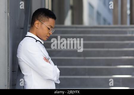 Dottore femminile stanco dopo una dura giornata in clinica, una donna afroamericana in clinica con grave mal di testa, e depressione dopo un lavoro eccessivo Foto Stock
