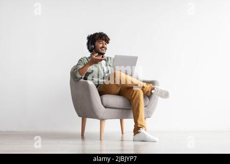 Positivo bello indiano che ha videoconferenza, usando il taccuino Foto Stock