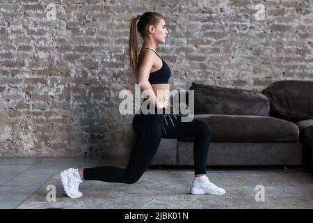 Vista del profilo della ragazza sportiva che fa gli affondi che allenano i muscoli delle gambe e i glutei in loft interno. Foto Stock