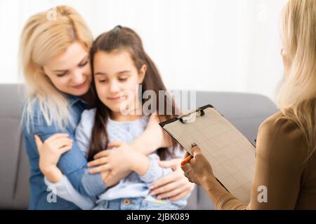 Mano di uno psicoterapeuta professionale di famiglia che scrive note davanti ad una famiglia con un bambino durante una consultazione Foto Stock