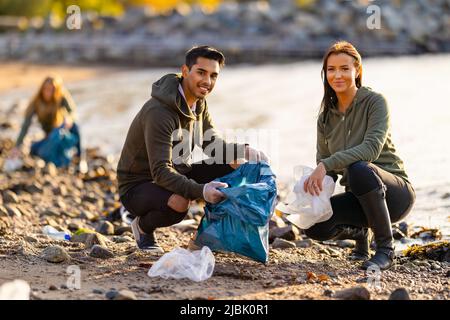 Team di volontari dedicati e sorridenti che raccolgono rifiuti di plastica in spiaggia Foto Stock