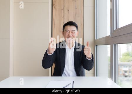 ritratto di giovane asiatico felice lavoratore maschile ufficio guardando la macchina fotografica e sorridendo in interni. Primo piano di un manager amichevole in un abito formale e bianco shir Foto Stock