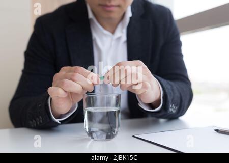 Primo piano di uomo d'affari in ufficio tenere pillole e bicchiere di acqua fresca, prendendo medicina per mal di testa, dolore addominale o prendere vitamine, salute Foto Stock