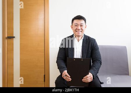 Uomo d'affari asiatico maschio ha ricevuto buone notizie, si rallegra nella sala d'attesa per un'intervista, vicino alla reception di un moderno centro affari Foto Stock