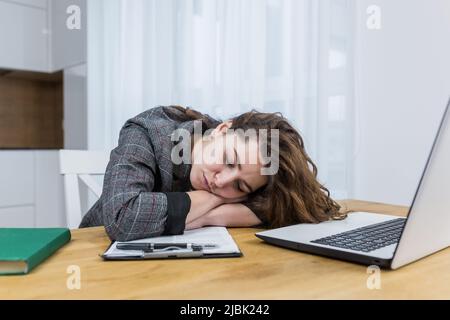 Una giovane studentessa si addormentò stanca al tavolo mentre studiava, a casa con un computer portatile e dei libri Foto Stock