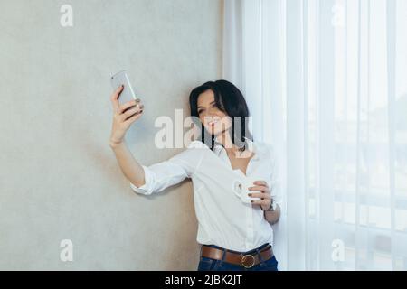 Bella giovane donna lavora a studiare a casa, si alza parlando al telefono. Conduce negoziati commerciali, colloqui con gli amici, bevande caffè Foto Stock