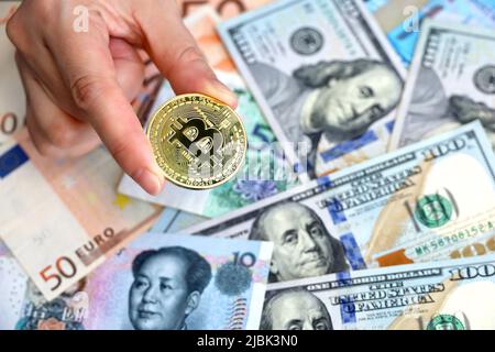 Bitcoin in mano femminile su sfondo di dollari USA, euro e yuan banconote. Moneta elettronica decentrata, tasso di cambio Foto Stock