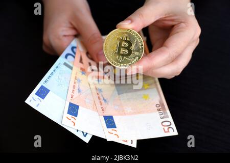 Banconote in Bitcoin e euro in mani femminili su sfondo scuro. Moneta elettronica decentralizzata, cripto-valuta Foto Stock