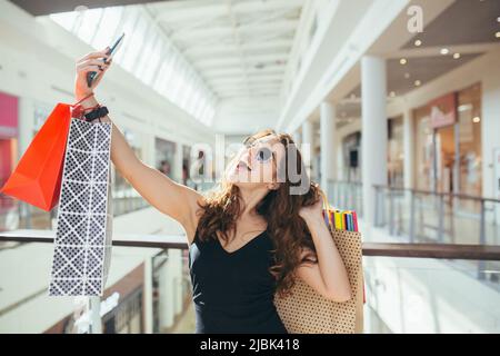 Felice giovane bella donna chiama sul videotelefono e mostra borse shopping fatto nel centro commerciale, prende selfie, ama lo shopping e nuovi vestiti. Sorridente Foto Stock