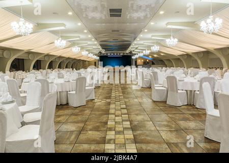 Grande sala banchetti decorata per eventi sociali con tavoli serviti e palco sullo sfondo Foto Stock