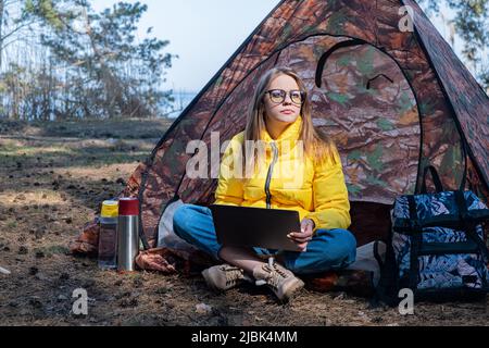 Formazione a distanza online e lavoro. Donna ragazza lavoro ufficio lavoro a distanza da sittin foresta in tenda. Utilizzando un computer portatile o un computer Foto Stock