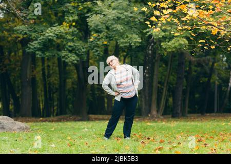 Donna anziana in piedi e fare sport nel parco sull'erba, esercitandosi, conducendo uno stile di vita attivo sano Foto Stock