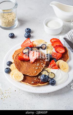 Colazione estiva. Pancake con fragole, mirtilli, banana e panna su un piatto bianco. Ricetta vegana. Foto Stock