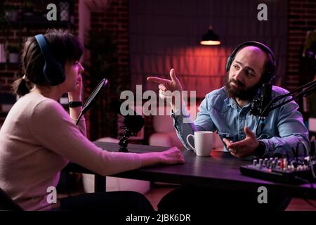 Presentatore maschile intervistando donna su podcast discussione, parlando con ospite in studio. Giovane che ha conversato con i social media blogger, programma di registrazione per i contenuti del canale. Foto Stock