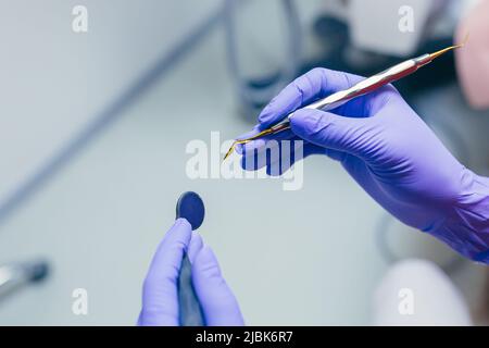 Primo piano le mani del medico fotografico in guanti medici blu che tengono in mano strumenti dentistici medici, preparandosi per il trattamento Foto Stock