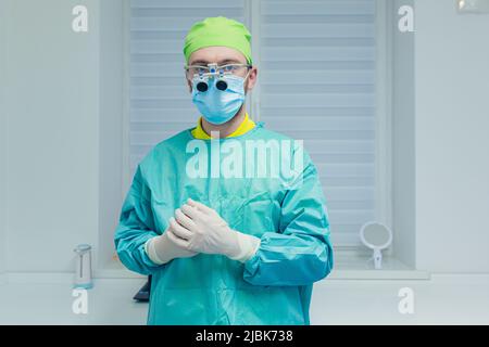 Ritratto di giovane medico maschile con microscopio in uniforme medica, maschera, in piedi, guardando la macchina fotografica in ufficio Foto Stock