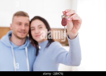 Ritratto di una giovane coppia, di un uomo e di una donna che si trasferirono in un nuovo appartamento. Casa, tenere le chiavi, abbracciando, sorridendo Foto Stock