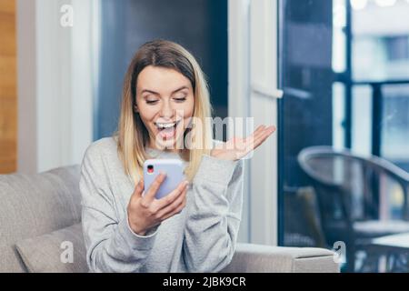 Ritratto di una bella ragazza felice che guarda il telefono ed è felice di aver vinto il premio, ha imparato la buona notizia Foto Stock