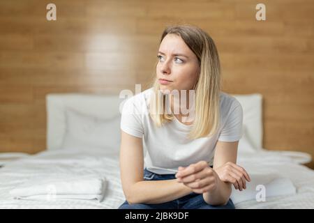 Giovane bella donna a casa seduta sul divano, tenendo un test di gravidanza veloce nelle sue mani, sconvolto, scioccato, imparato la gravidanza, pensa confu Foto Stock