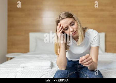 Giovane bella donna a casa seduta sul divano, tenendo un test di gravidanza veloce nelle sue mani, sconvolto, scioccato, imparato la gravidanza, pensa confu Foto Stock