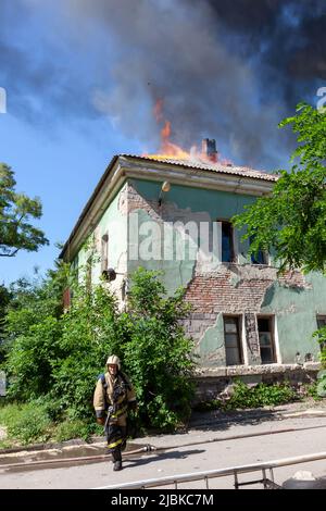 Russia, Rostov-on-Don - 2 giugno 2022: Un vigile del fuoco corre sullo sfondo di una casa in fiamme. Foto Stock