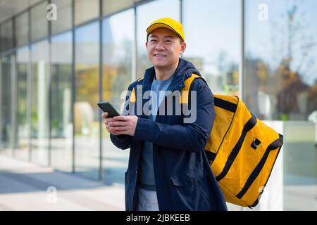 Buon fornitore di cibo a piedi corriere maschio, in attesa di nuovo ordine ricevuto in app telefono, corriere asiatico Foto Stock