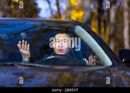 Furioso uomo asiatico arrabbiato in piedi in un traffico jam bip e uragani. Seduto in auto. Irritato giovane uomo d'affari conducente stanco in automobile. Str Foto Stock