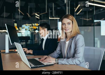 Ritratto di donna di successo, membro del team aziendale, donna d'affari che guarda la fotocamera e sorride lavorando sul laptop in un ufficio moderno Foto Stock