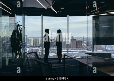 Silhouette di due dipendenti team di uomini d'affari, asiatici uomo e donna sono di consulenza e comunicazione, lavorando in un ufficio moderno dalla finestra Foto Stock