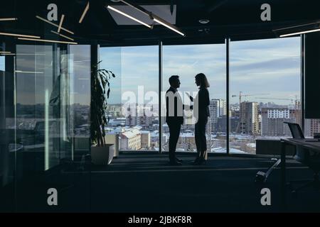 Silhouette di due dipendenti team di uomini d'affari, asiatici uomo e donna sono di consulenza e comunicazione, lavorando in un ufficio moderno dalla finestra Foto Stock