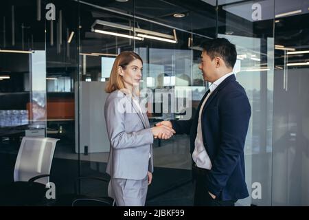 Due partner commerciali hanno raggiunto un accordo e scuotere le mani, uomini d'affari, uomo asiatico e donna caucasica, affari periti Foto Stock