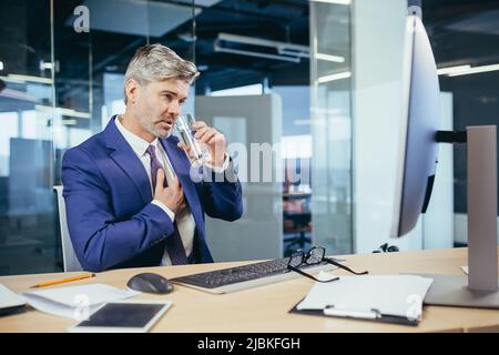 L'uomo d'affari dai capelli grigi ha un dolore toracico severo, un lavoratore esperto che lavora ad una scrivania nell'ufficio Foto Stock