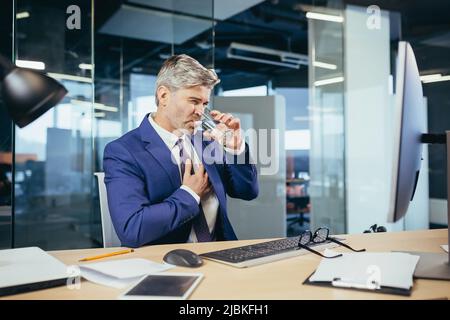 L'uomo d'affari dai capelli grigi ha un dolore toracico severo, un lavoratore esperto che lavora ad una scrivania nell'ufficio Foto Stock