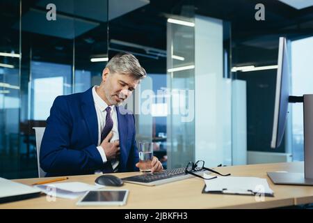 L'uomo d'affari dai capelli grigi ha un dolore toracico severo, un lavoratore esperto che lavora ad una scrivania nell'ufficio Foto Stock