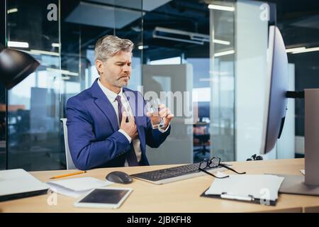 L'uomo d'affari dai capelli grigi ha un dolore toracico severo, un lavoratore esperto che lavora ad una scrivania nell'ufficio Foto Stock